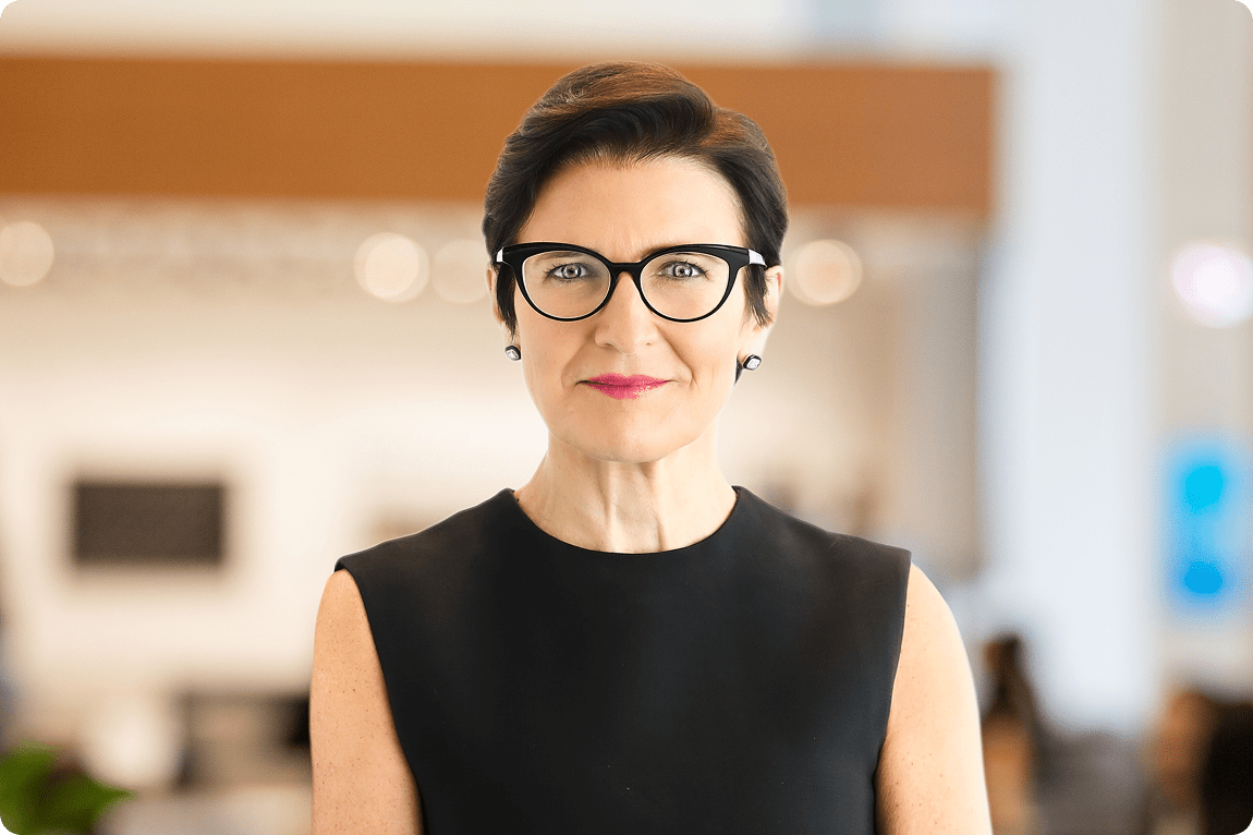 Jane Fraser, DBE, Chair and Chief Executive Officer, smiling, wearing glasses and a black top