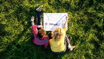 Two children seated on the grass reading a map.